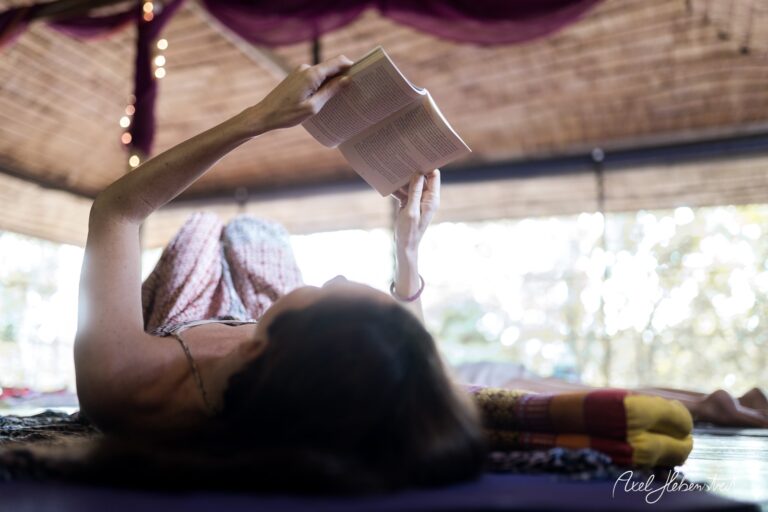 Eine Frau liegt entspannt auf dem Boden und liest ein Buch in einem lichtdurchfluteten Yogaraum – © Axel Hebenstreit