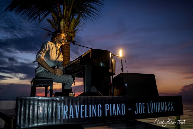 Ein Pianist spielt bei Sonnenuntergang am Strand, umgeben von Palmen, eine entspannte und inspirierende Atmosphäre. – © Axel Hebenstreit