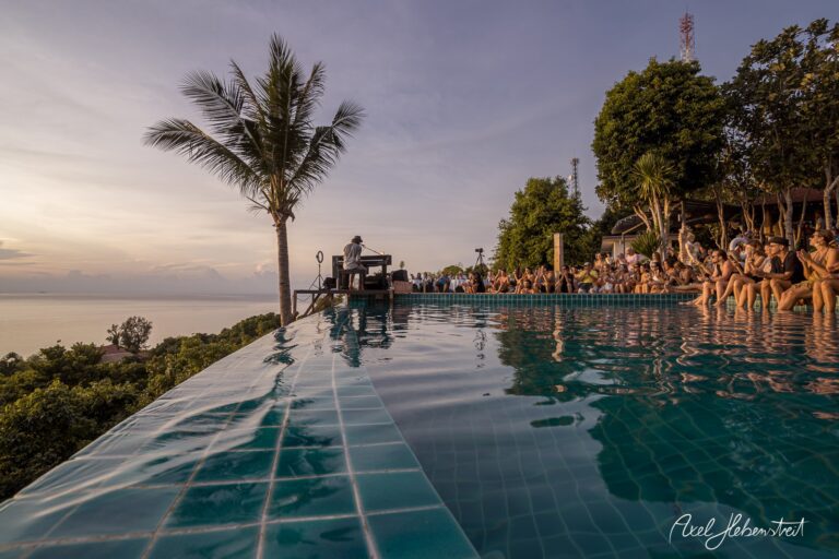 Ein Musiker spielt am Rand eines Infinity-Pools bei Sonnenuntergang, umgeben von einem begeisterten Publikum – © Axel Hebenstreit