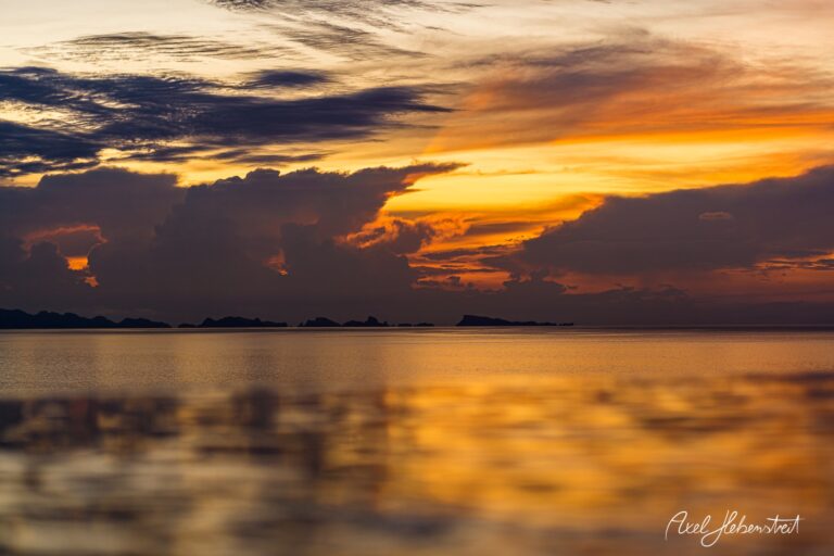 Sonnenuntergang über ruhigem Wasser, während Wolken in leuchtenden Farben reflektieren – © Axel Hebenstreit