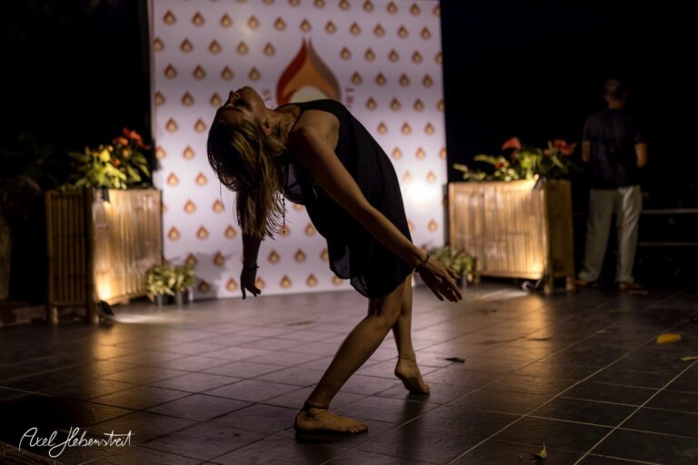 Eine Tänzerin in einer ausdrucksvollen Pose auf einer Bühne im Freien, umgeben von stimmungsvollem Licht – © Axel Hebenstreit