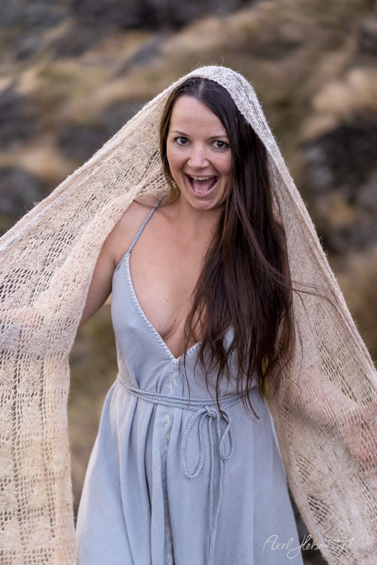 Eine fröhliche Frau in einem hellen Kleid mit einem transparenten Schal, die im Freien posiert und lächelt. – © Axel Hebenstreit