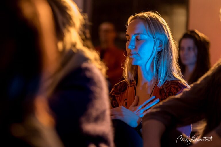 Eine meditierende Frau mit geschlossenen Augen und sanfter Beleuchtung in einer Yoga-Umgebung – © Axel Hebenstreit