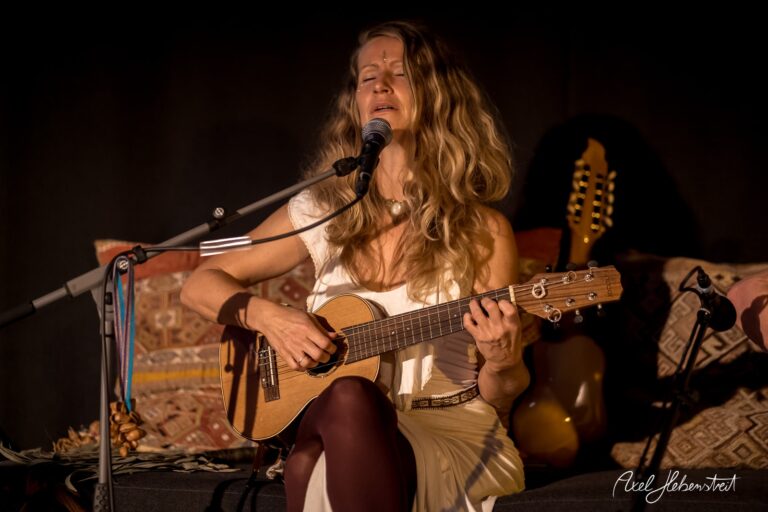 Frau spielt gefühlvoll Ukulele und singt in einer stimmungsvolle Atmosphäre auf einer Bühne – © Axel Hebenstreit