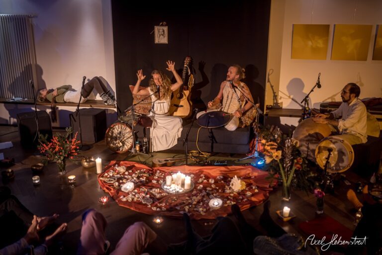 Musiker spielen live auf einer kleinen Bühne, umgeben von Kerzen und Blumen, in einer gemütlichen Atmosphäre – © Axel Hebenstreit