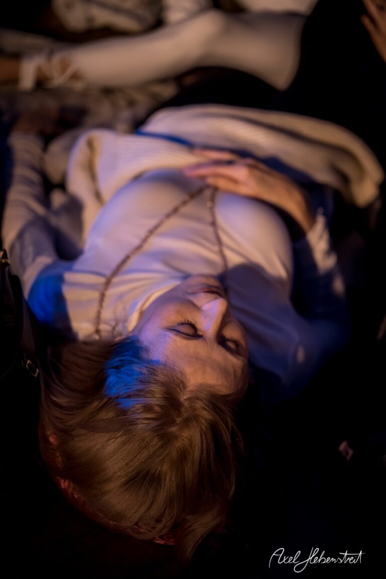 Eine liegende Person mit nachdenklichem Ausdruck, umgeben von sanftem Licht auf einem Festival. – © Axel Hebenstreit