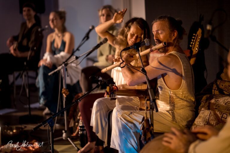Ein Musiker spielt auf einer Flöte während eines intimen Konzerts, umgeben von einer entspannten Gruppe. – © Axel Hebenstreit