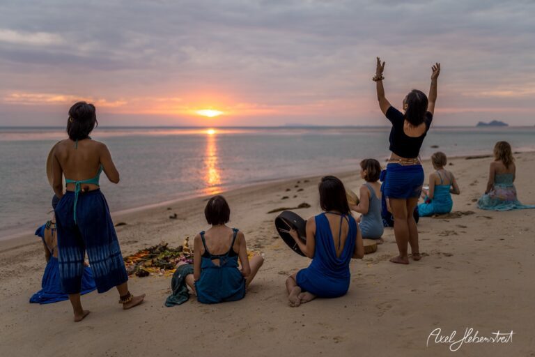 Frauen in blauen Kleidern feiern den Sonnenuntergang am Strand und schaffen eine spirituelle Atmosphäre – © Axel Hebenstreit.