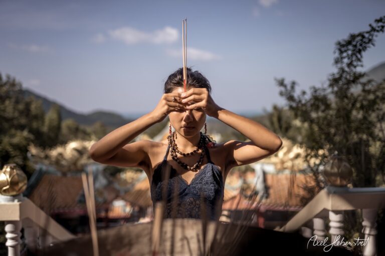 Junge Frau in einem spirituellen Moment mit Räucherstäbchen, umgeben von Natur und Bergen – © Axel Hebenstreit