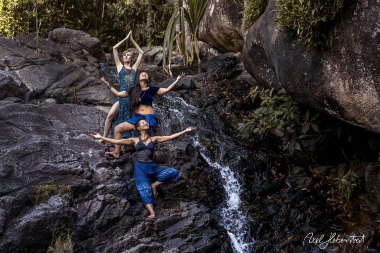 Drei Frauen in Meditationspose in der Natur, umgeben von Felsen und Wasserfall – © Axel Hebenstreit