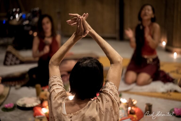 Frauen praktizieren eine spirituelle Zeremonie im Kerzenschein, umgeben von kulturellen Symbolen – © Axel Hebenstreit