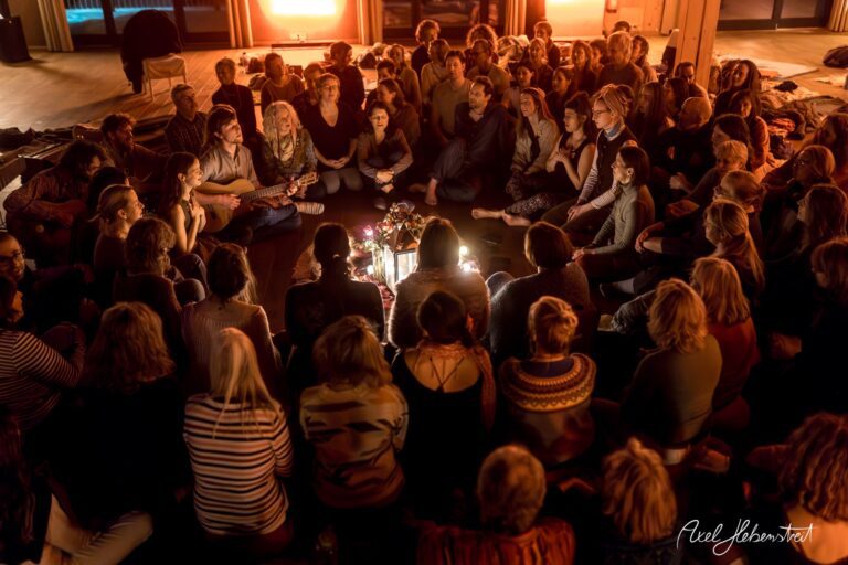 Eine Gruppe von Menschen sitzt im Kreis um ein Licht, während sie gemeinsam singen und musizieren – © Axel Hebenstreit