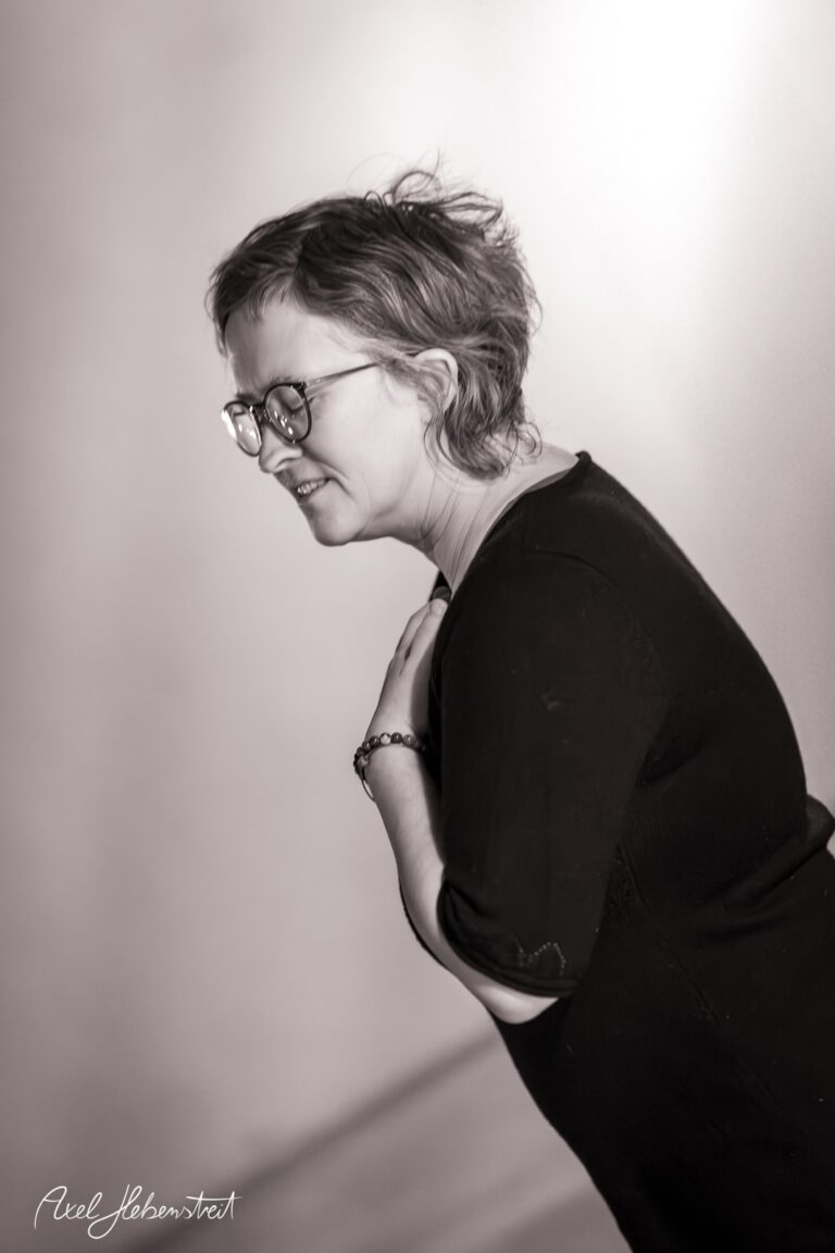 Eine lächelnde Frau mit Brille neigt sich leicht zur Seite und strahlt Freude aus. – © Axel Hebenstreit