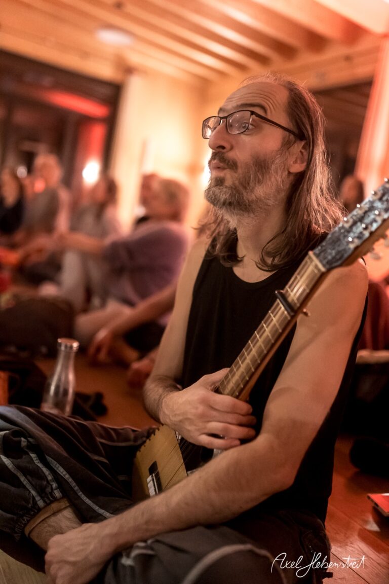 Musiker in entspannten Zügen spielt ein Instrument in einer warmen, einladenden Atmosphäre – © Axel Hebenstreit