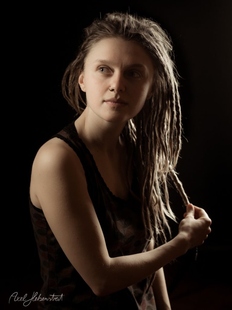 Porträt einer Frau mit Dreadlocks vor schwarzem Hintergrund, nachdenkliche Blickrichtung – © Axel Hebenstreit