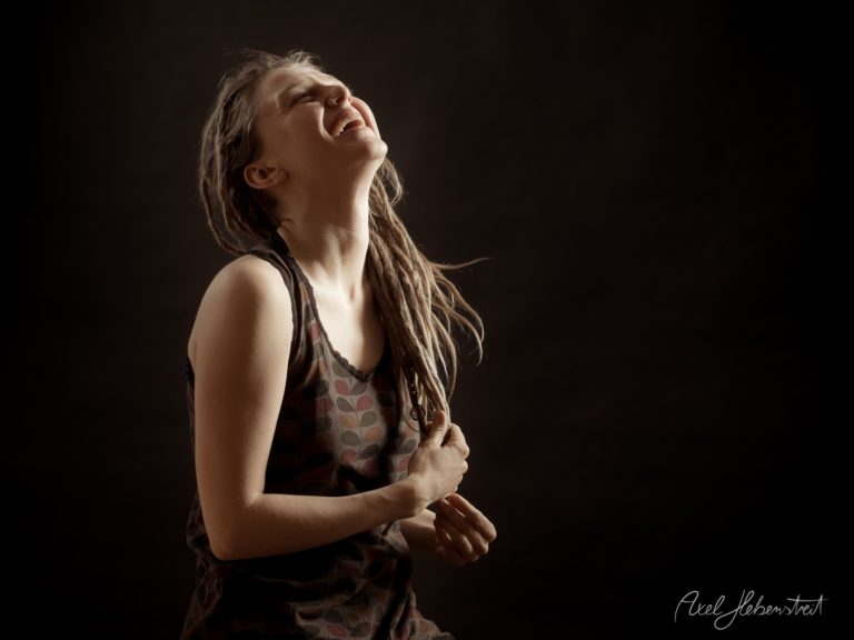 Junge Frau mit Dreadlocks blickt nach oben in emotionaler Pose vor dunklem Hintergrund – © Axel Hebenstreit