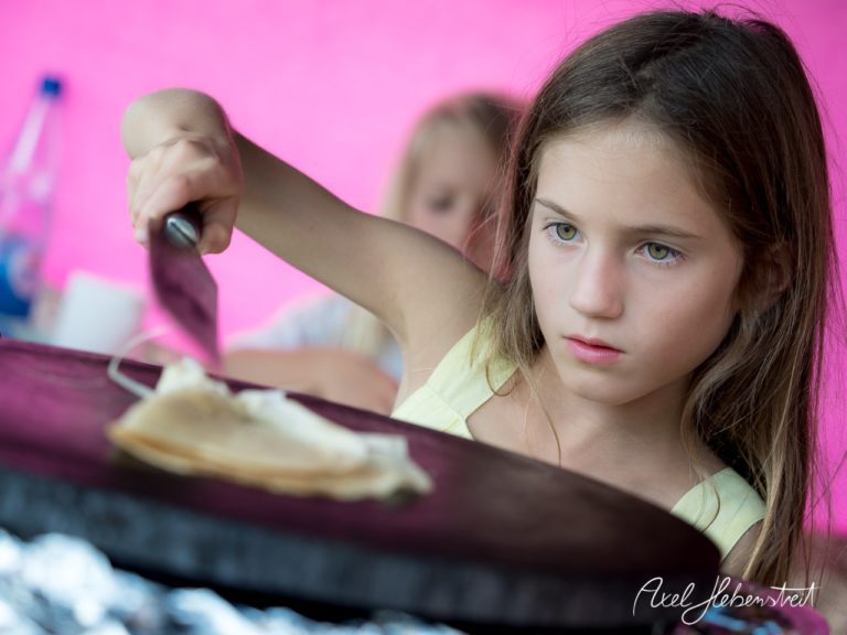 Ein Mädchen bereitet konzentriert eine Crépe an einem heißen Crepe-Platte während eines Festivals vor. – © Axel Hebenstreit