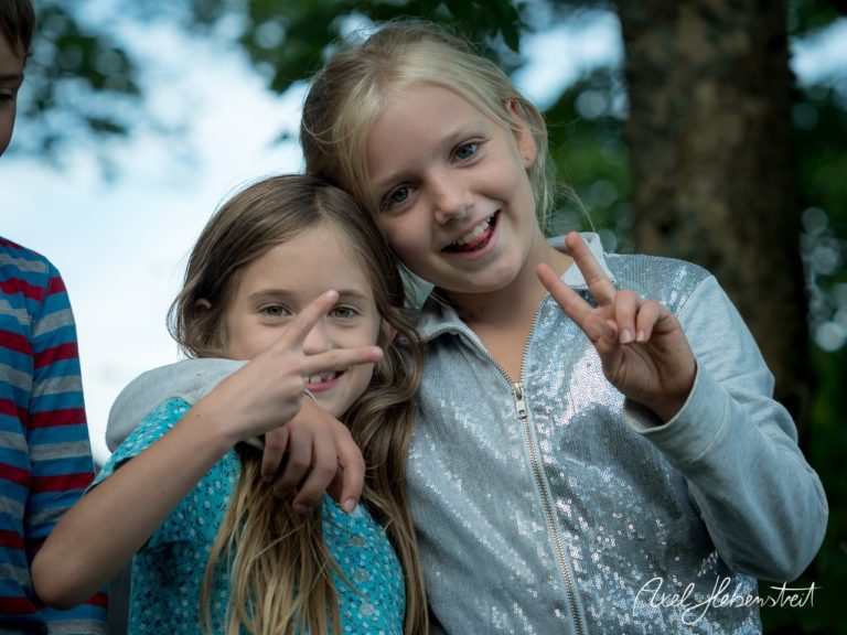 Zwei fröhliche Mädchen zeigen Peace-Zeichen und lachen zusammen im Freien. – © Axel Hebenstreit