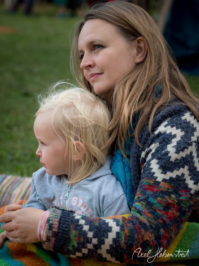 Eine Frau umarmt ein kleines Kind, beide schauen in die Ferne, umgeben von einer entspannten Festivalatmosphäre. – © Axel Hebenstreit