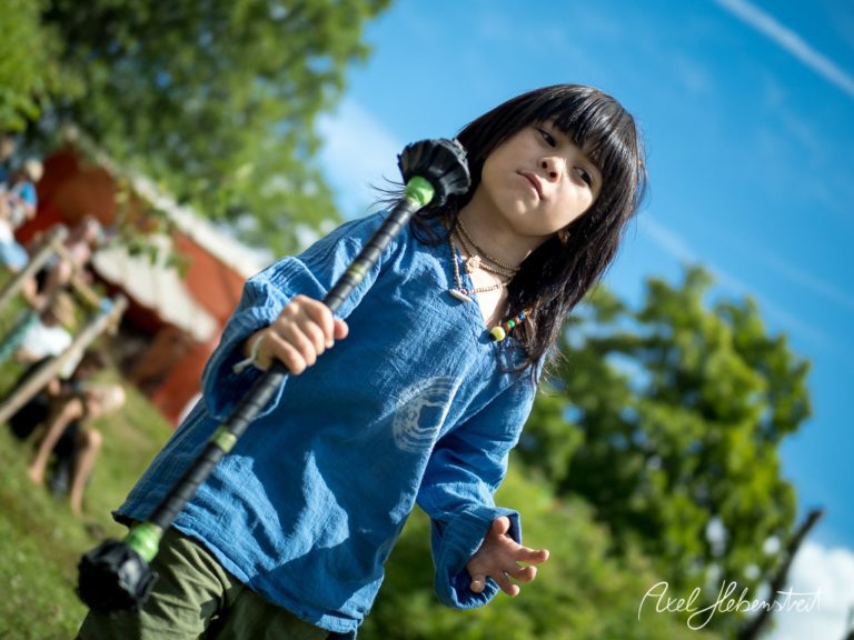 Ein Junge in einem blauen Shirt hält einen Stock und schaut konzentriert in der Natur während eines Festivals. – © Axel Hebenstreit