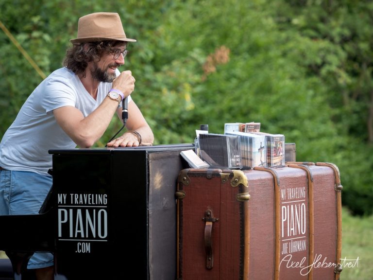 Ein Musiker spricht am Klavier auf einem Festival im Freien und begeistert das Publikum mit seiner Performance – © Axel Hebenstreit