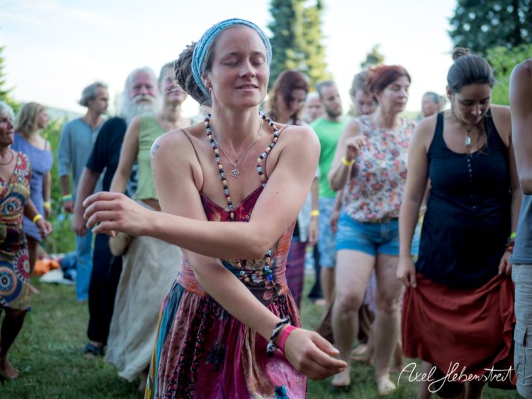Tanzende Menschen in fröhlicher Atmosphäre bei einem Festival im Freien, umgeben von Natur. – © Axel Hebenstreit