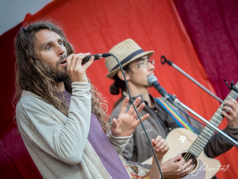 Zwei Musiker begleiten einen Gesang mit akustischer Gitarre auf einer Bühnenaufführung bei einem Festival. – © Axel Hebenstreit