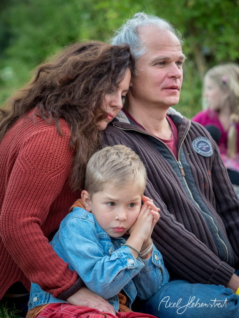 Eine Familie sitzt eng beieinander in einer naturnahen Umgebung, zeigt Zuneigung und Geborgenheit. – © Axel Hebenstreit