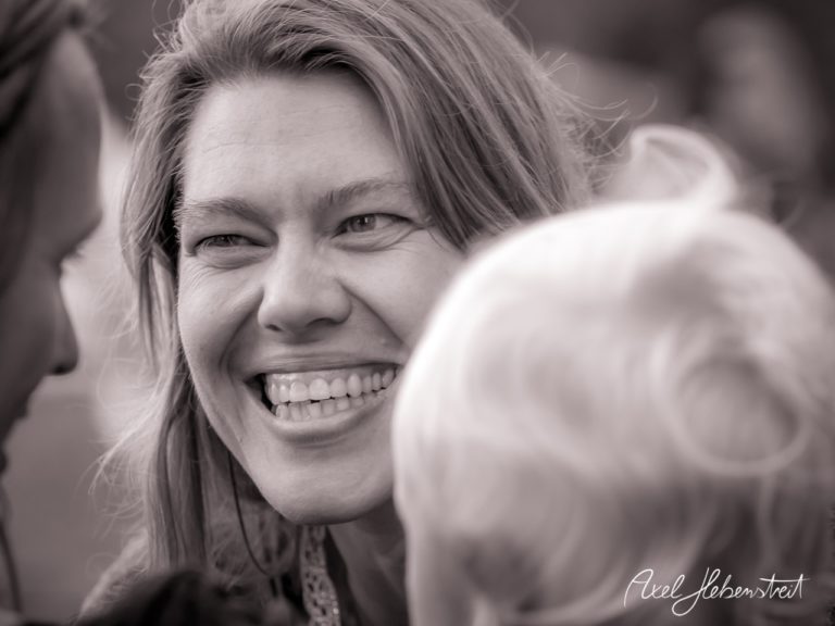 Eine lächelnde Frau, umgeben von lieben Menschen, strahlt Freude und Verbundenheit aus – © Axel Hebenstreit