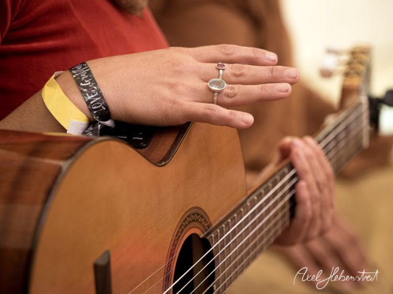 Hände eines Musikers, die Gitarre spielend, vermitteln eine entspannte Atmosphäre in einem geschützten Raum. – © Axel Hebenstreit
