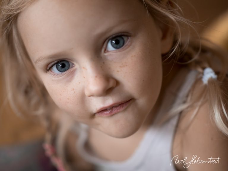 Ein kleines Mädchen mit blauen Augen und Sommersprossen schaut neugierig in die Kamera. – © Axel Hebenstreit
