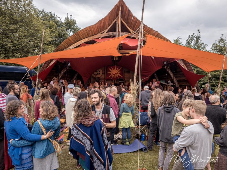 Menschen versammeln sich in fröhlicher Stimmung um eine Bühne bei einem Festival inmitten der Natur. – © Axel Hebenstreit