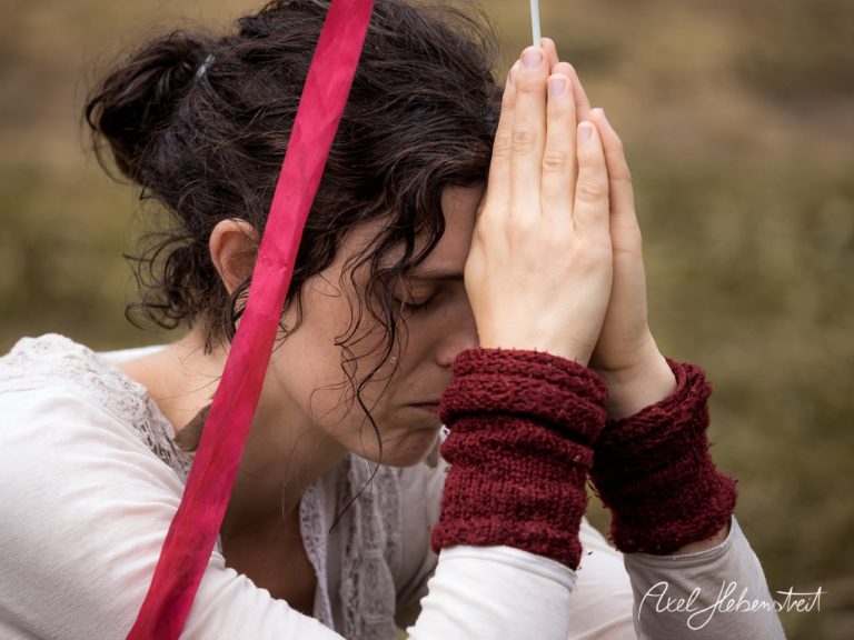 Frau mit geschlossenen Augen und gefalteten Händen in einer meditativen Pose, umgeben von Natur. – © Axel Hebenstreit