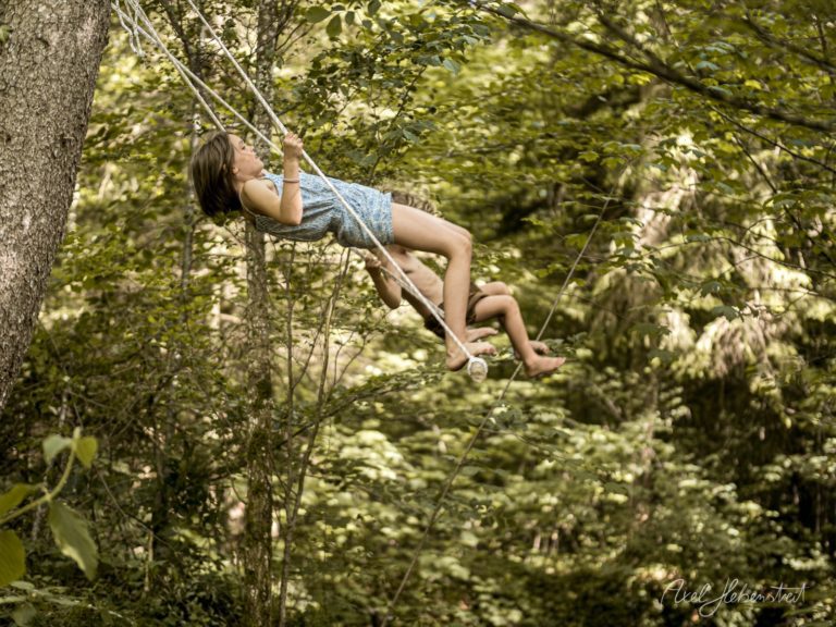 Junge Frau schwingt sich an einem Seil durch üppig grünen Wald in sommerlicher Freiheit – © Axel Hebenstreit