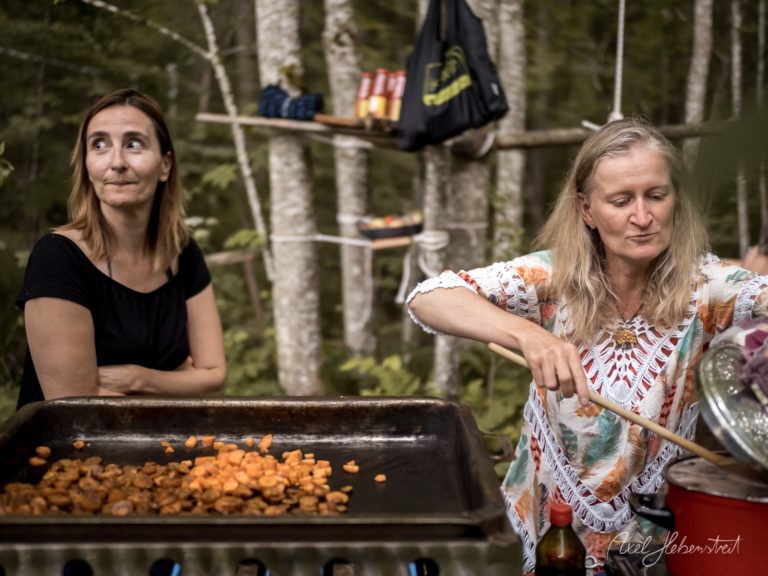 Zwei Frauen bereiten traditionelles Essen in einer Schüssel bei einem Outdoor-Festival im Wald zu – © Axel Hebenstreit