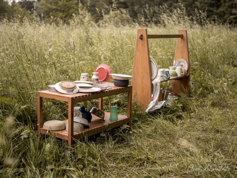 Rustikale Picknick-Station mit Holzmöbeln und Geschirr in einer blütenreichen Wildblumenwiese – © Axel Hebenstreit