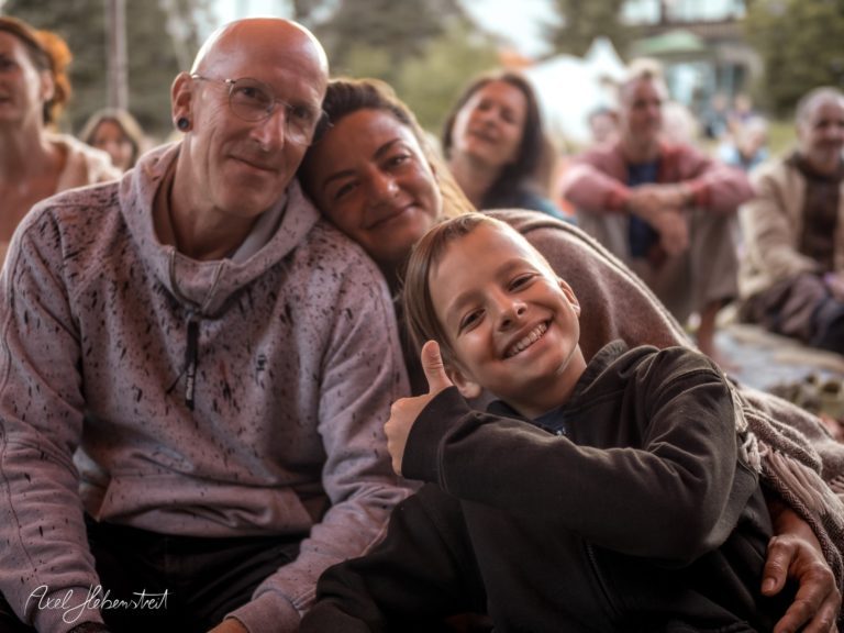 Lächelnde Familie mit einem Jungen, der Daumen hoch zeigt, in fröhlicher Festival-Atmosphäre – © Axel Hebenstreit
