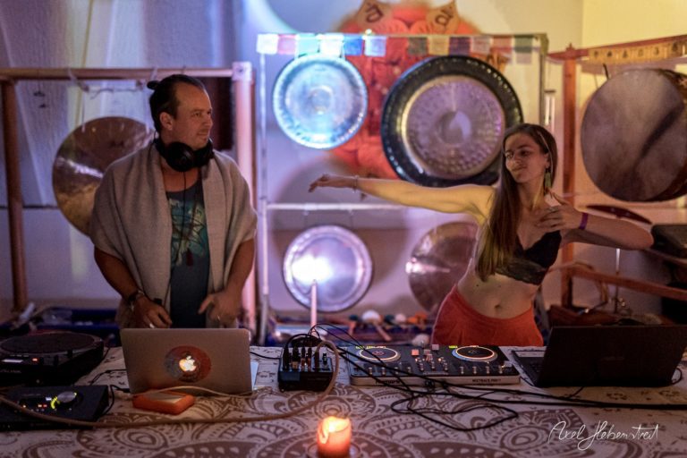 DJ und Tänzerin vor einer Wand aus Gongs, die eine entspannte, atmosphärische Stimmung vermitteln – © Axel Hebenstreit