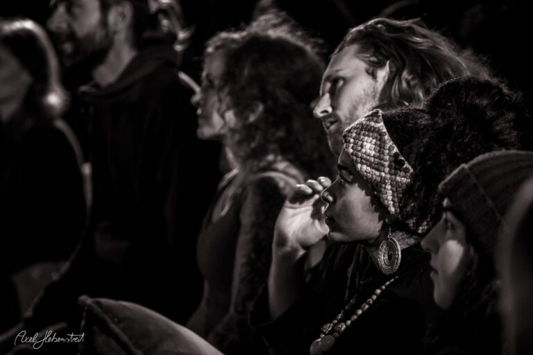 Eine Gruppe von Menschen in engem Raum lauscht aufmerksam einem Auftritt, Stimmung voller Konzentration und Emotion – © Axel Hebenstreit.