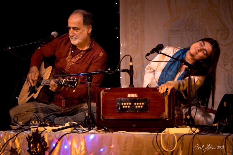 Zwei Musiker auf der Bühne spielen Gitarre und Harmonium, während eine entspannte Atmosphäre herrscht. – © Axel Hebenstreit