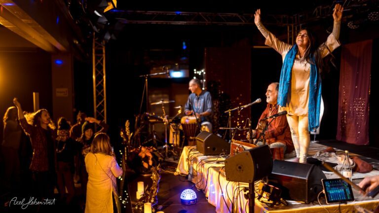 Eine Musikerin steht begeistert auf der Bühne, während das Publikum tanzend und mit Freude reagiert – © Axel Hebenstreit.
