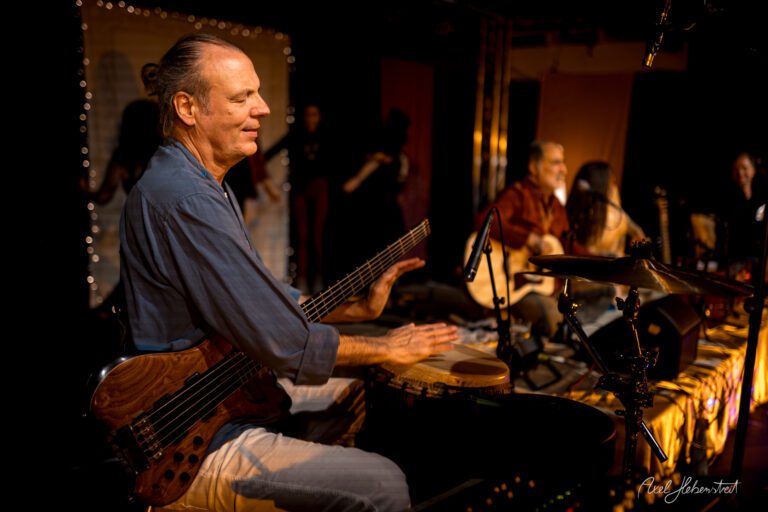 Ein Musiker spielt rhythmisch auf einem handgemachten Instrument während eines atmosphärischen Konzerts. – © Axel Hebenstreit