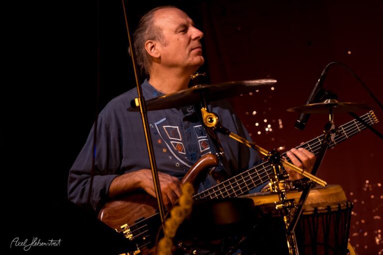 Ein Musiker spielt konzentriert am Bass auf der Bühne, umgeben von sanften Lichtakzenten – © Axel Hebenstreit