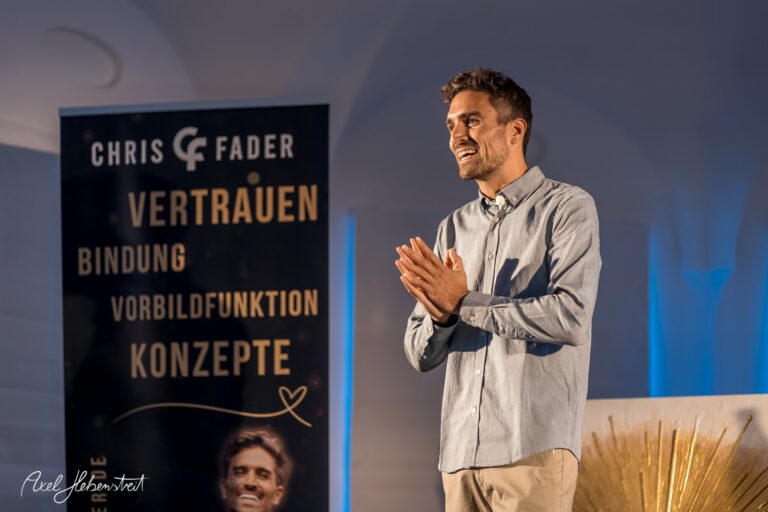 Ein Redner mit leidenschaftlicher Gestik präsentiert am Mikrofon auf einer Bühne, umgeben von Bannern. – © Axel Hebenstreit