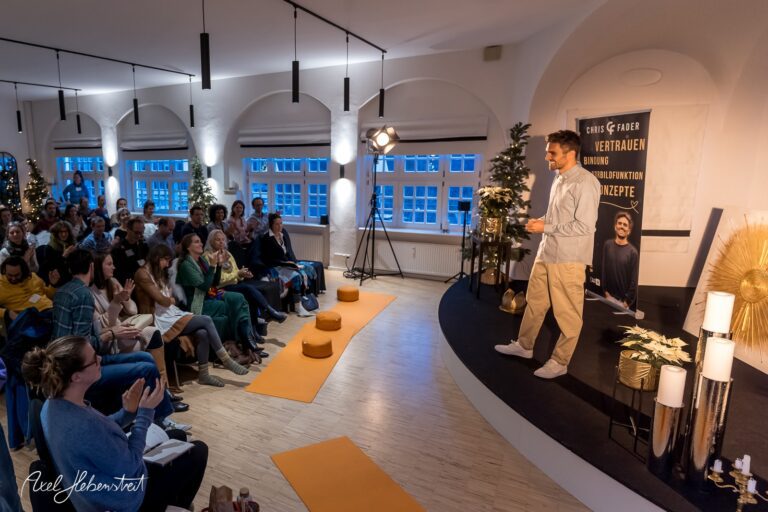 Ein Redner steht auf der Bühne vor einem Publikum in einem hellen Veranstaltungsraum, umgeben von festlicher Dekoration. – © Axel Hebenstreit