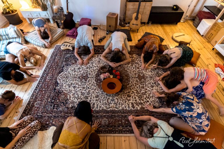 Gruppierung von Menschen in entspannter Yoga-Session auf einem Teppich in einem gemütlichen Innenraum – © Axel Hebenstreit