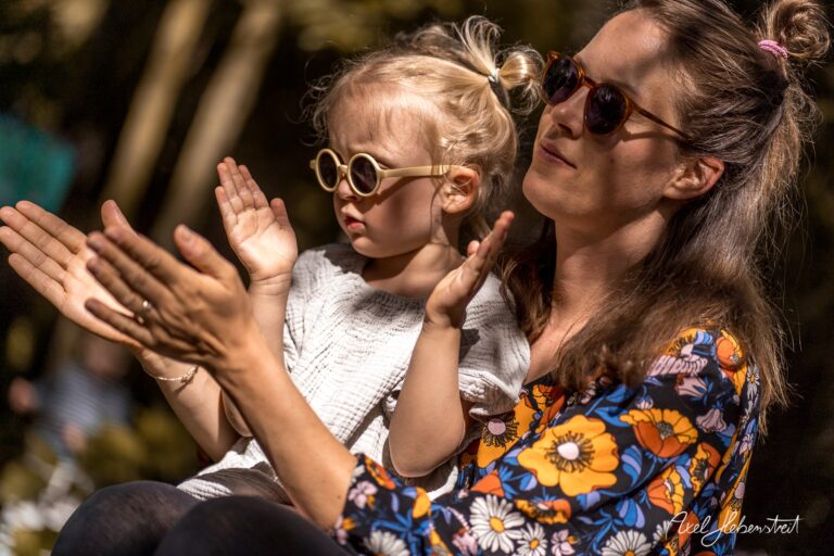 Eine Mutter und ihr Kind in Sonnenbrillen klatschen begeistert im Freien. – © Axel Hebenstreit