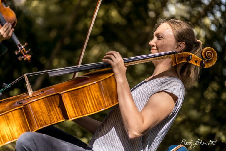 Eine Cellistin spielt konzentriert inmitten einer grünen Umgebung, die Stimmung ist entspannt und musikalisch – © Axel Hebenstreit.
