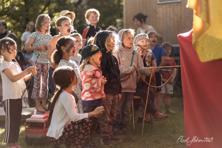 Gruppe begeisterter Kinder bei einer Aufführung im Freien, gespannt und fröhlich – © Axel Hebenstreit