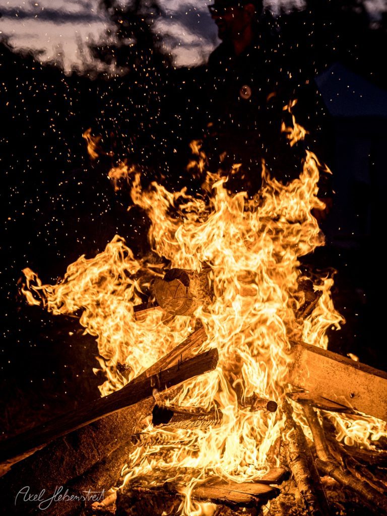 Loderndes Lagerfeuer bei Nacht mit intensiven Flammen und Funkenflug vor dunklem Himmel – © Axel Hebenstreit